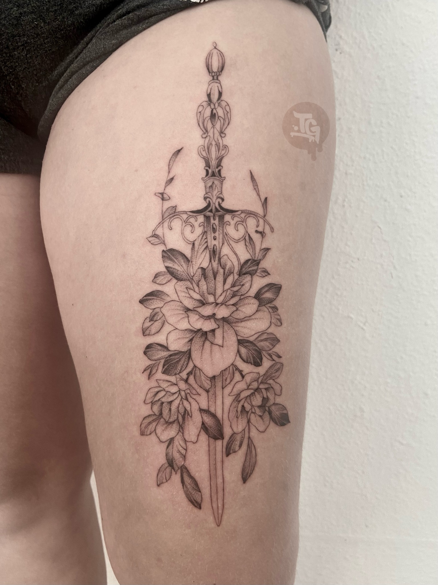 Ornamental dagger and floral thigh tattoo